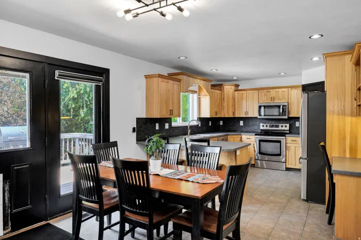 Kitchen featuring light wood cabinetry, stainless steel appliances, dark stone countertops, tile flooring, and recessed lighting