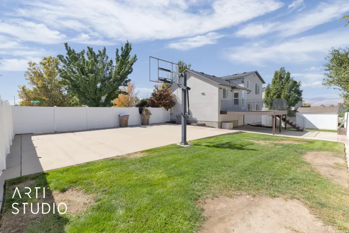 Spacious backyard featuring a large concrete pad, basketball hoop, and manicured lawn
