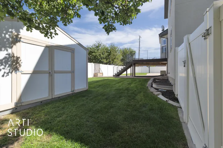 Expansive lawn featuring a storage shed, vinyl fencing, and a raised wood-finish deck with metal railings
