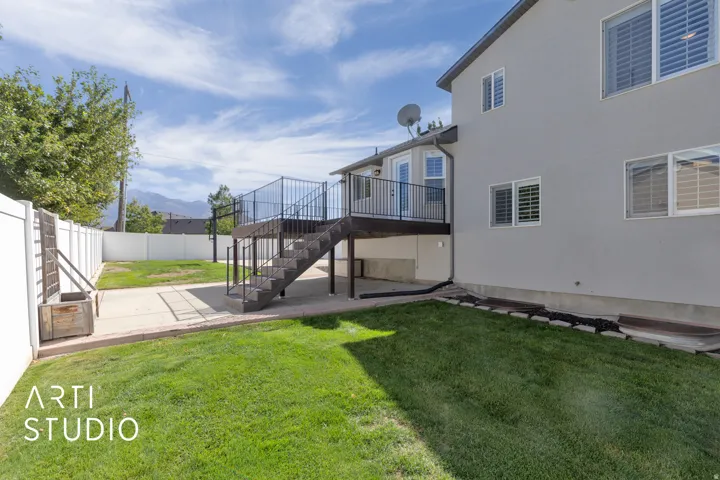 Expansive backyard featuring a manicured lawn, concrete patio, and white vinyl fencing
