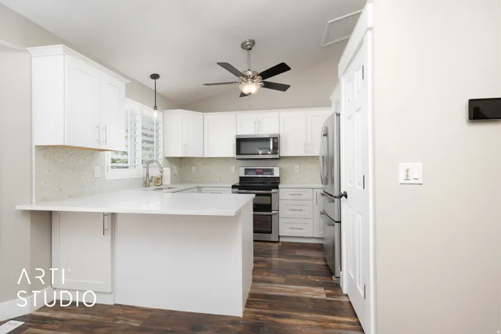 Contemporary kitchen featuring white cabinetry, light-toned backsplash, stainless steel appliances, wood-finish flooring, and a ceiling fan