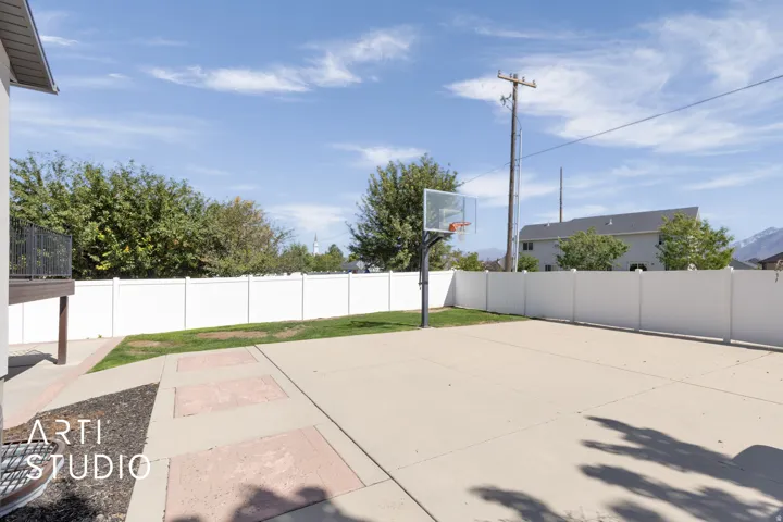Expansive concrete pad, ideal for recreation, featuring a basketball hoop, surrounded by a white privacy fence