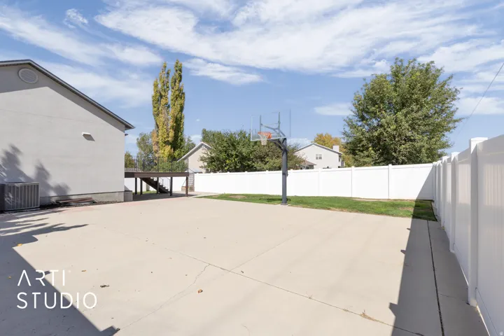 Expansive concrete patio area featuring a basketball hoop, white privacy fencing, and a raised wooden deck with stairs