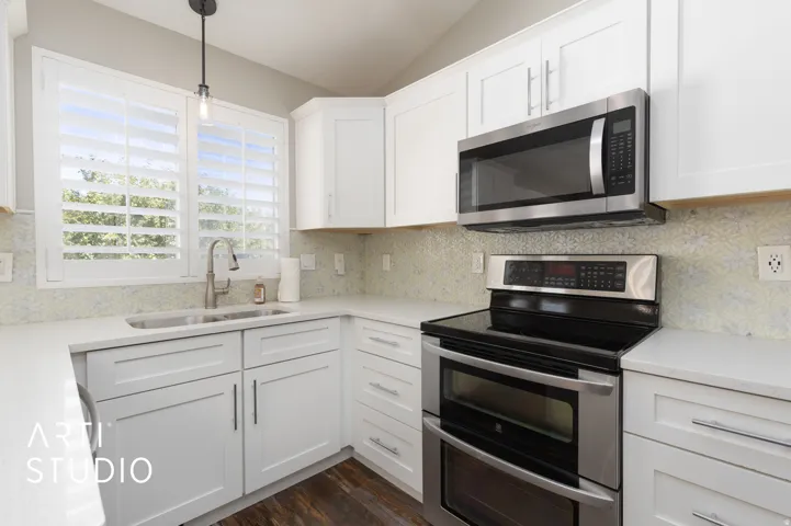 Modern kitchen featuring white shaker cabinetry, stainless steel appliances, light-toned countertops, decorative backsplash tiling, and wood-finish flooring