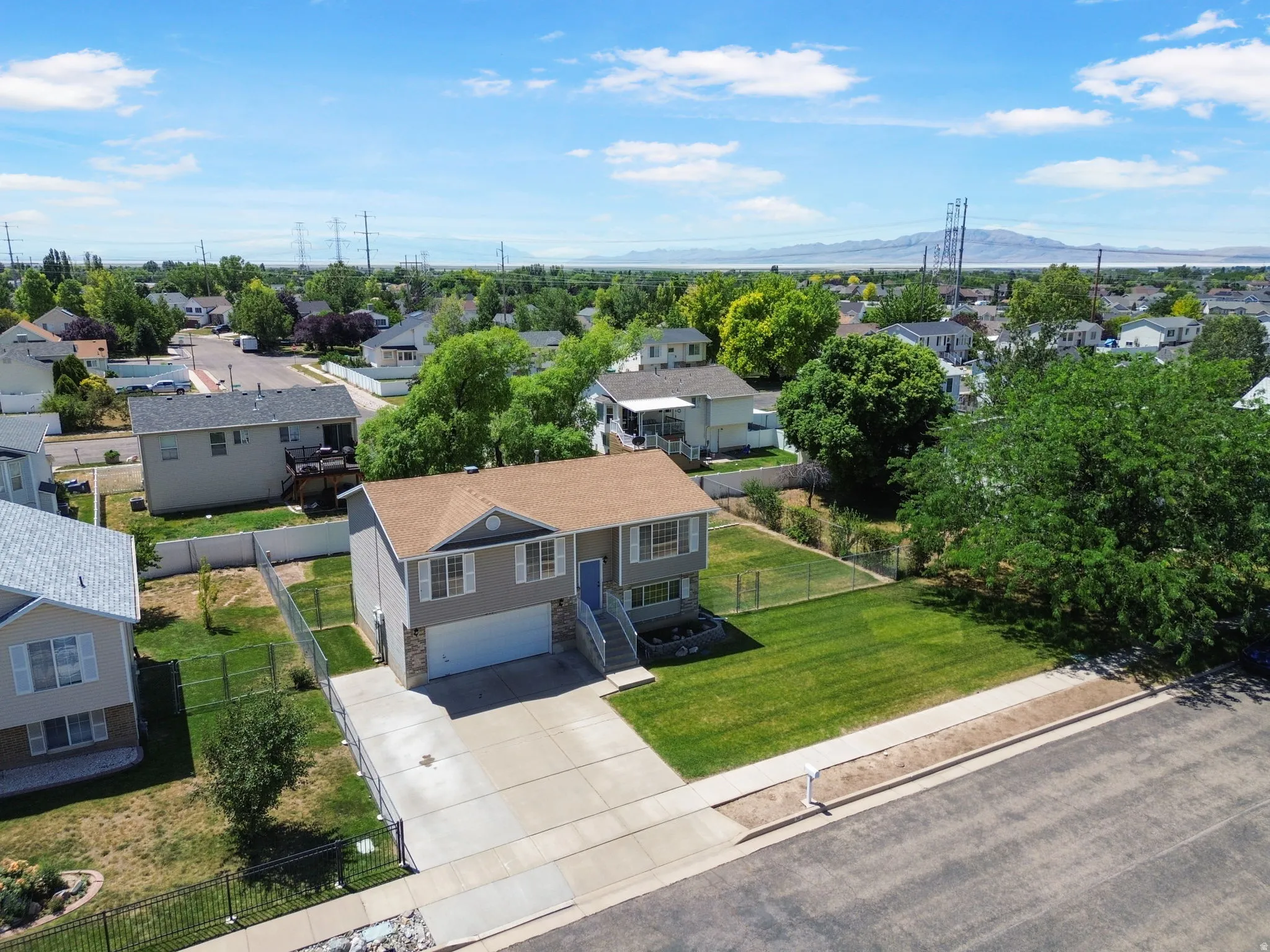 Split-level residence featuring a two-car garage, concrete driveway, and a fenced backyard with mature trees
