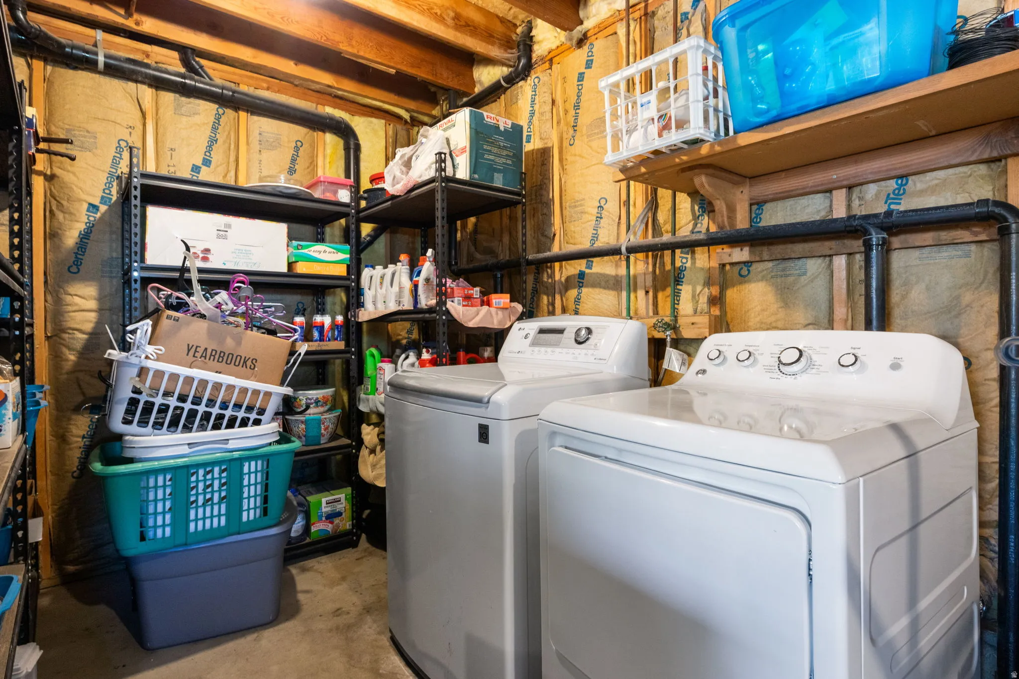 Dedicated laundry area featuring a white washing machine and dryer, exposed wood joists, black piping, and wall insulation