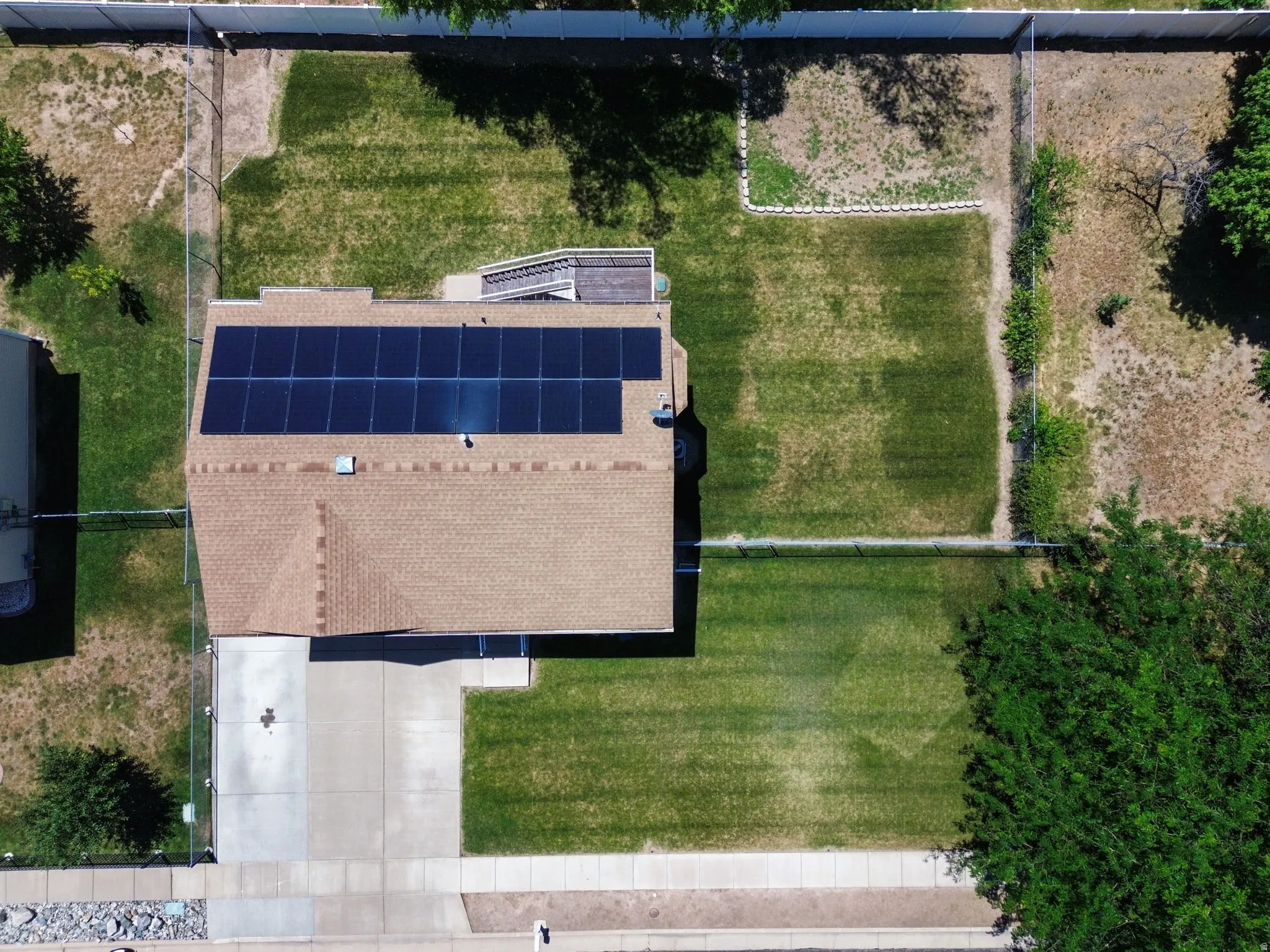 Shingle roof with solar panel array, concrete driveway, and expansive fenced backyard with lawn