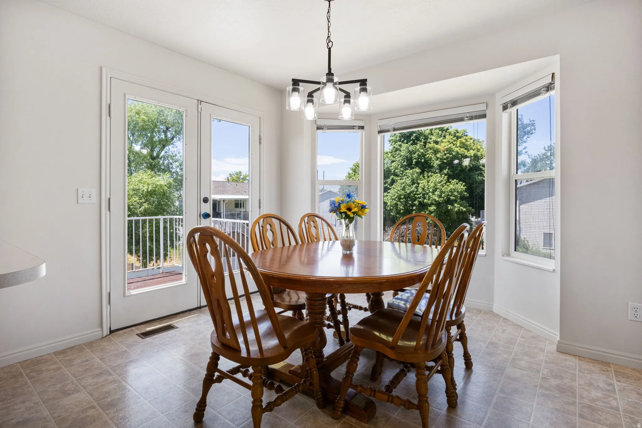 Bright dining space featuring a bay window, French doors, contemporary chandelier, and resilient tile flooring
