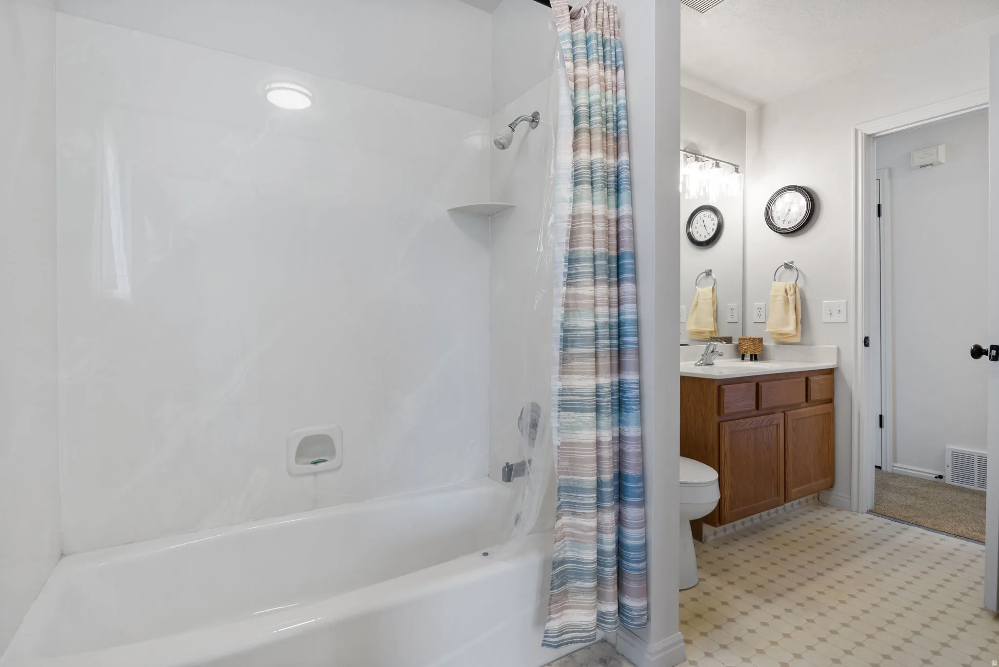 White bathtub and shower combination with an integrated corner shelf and recessed lighting