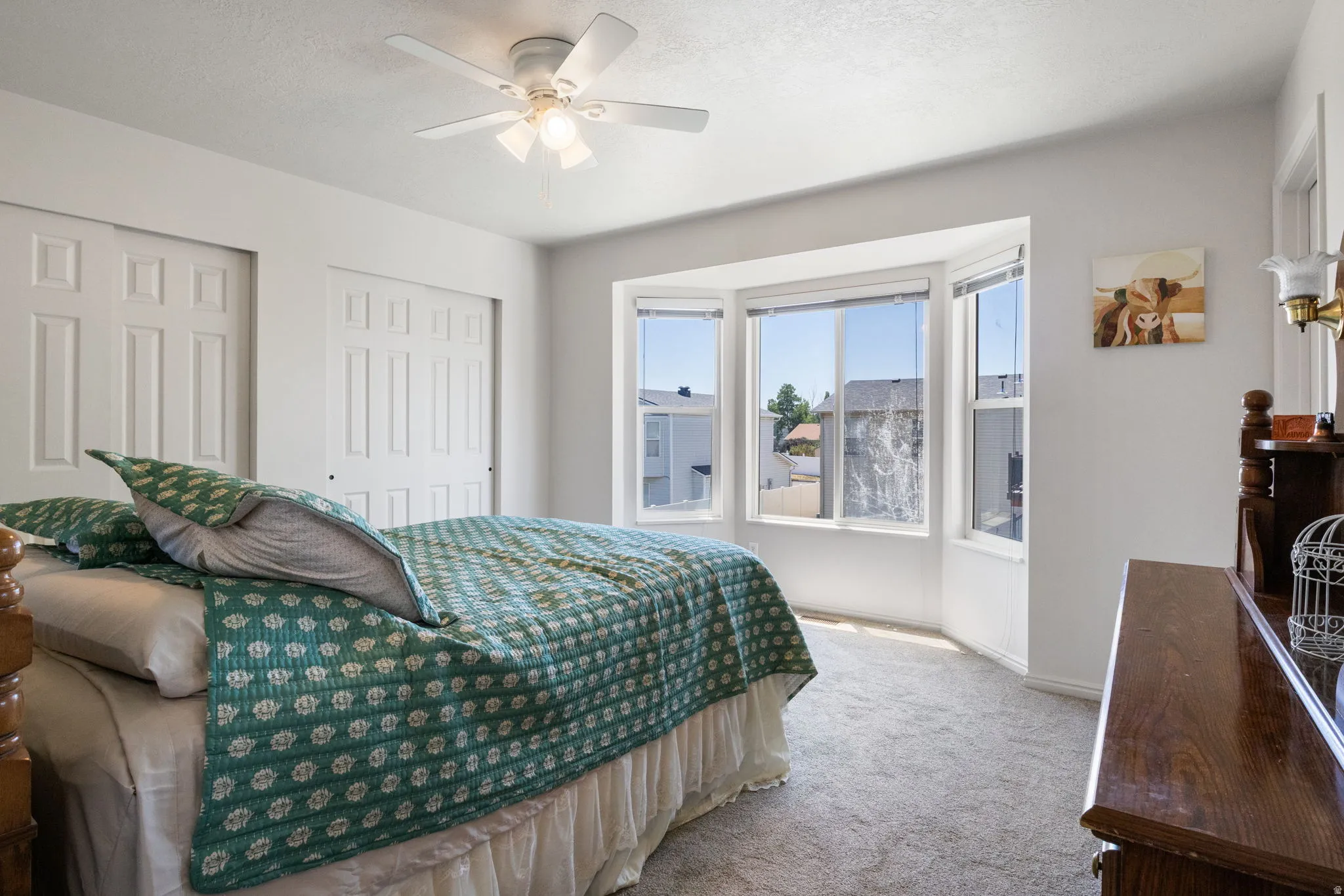 Bedroom featuring a multi-paned bay window, light grey carpet, a ceiling fan with integrated lighting, and two white bi-fold closet doors