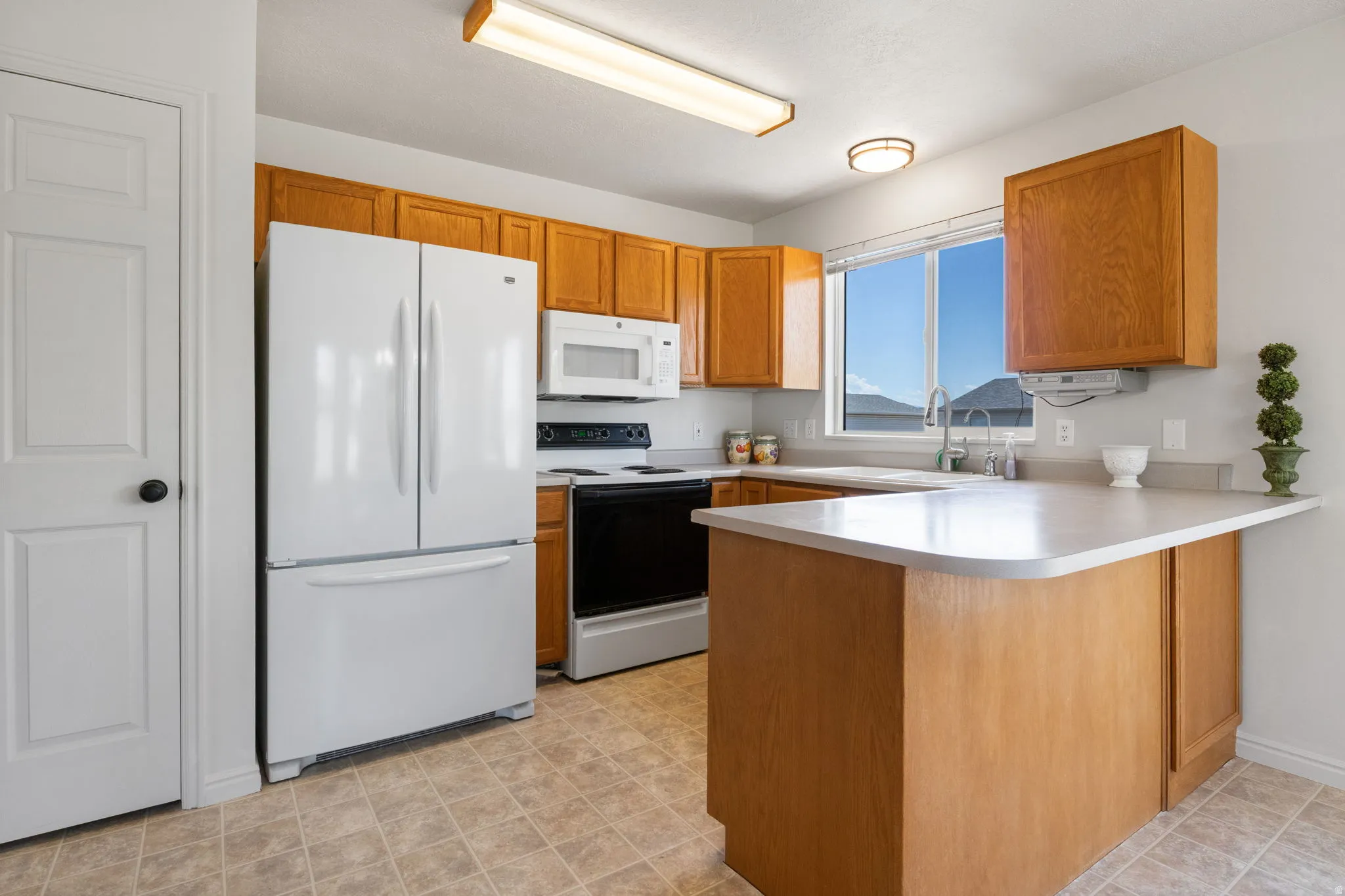 Kitchen featuring wood-finish cabinetry, white appliances, and a window above the sink
