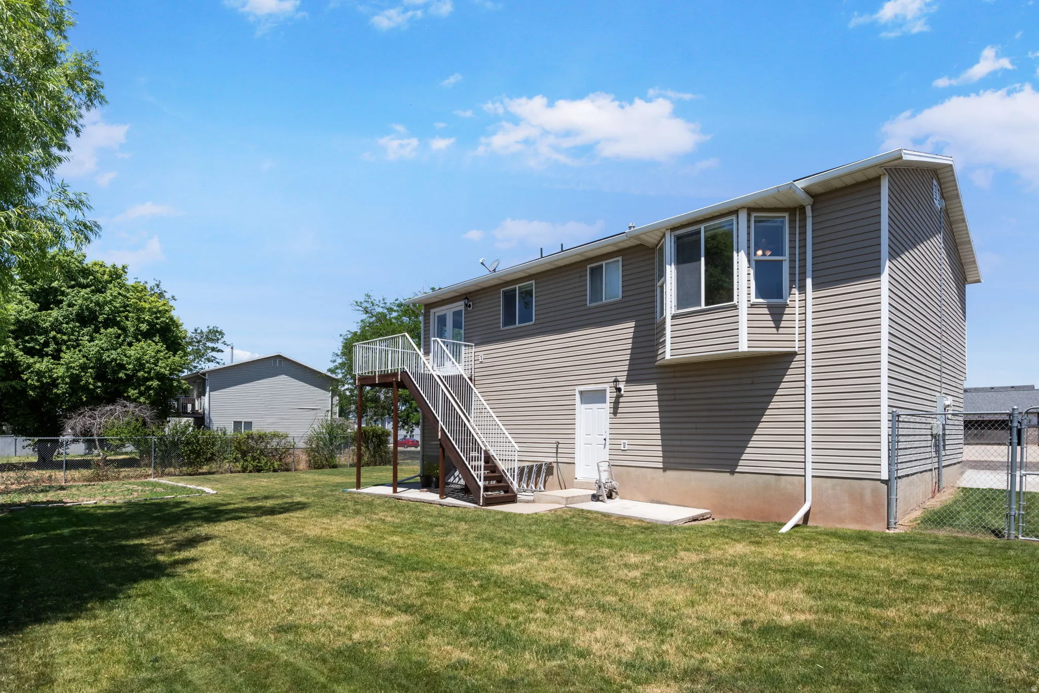 Expansive backyard featuring a manicured lawn, a two-story exterior with light-colored siding, a second-story deck with exterior stairs, a bay window, and a chain-link fence
