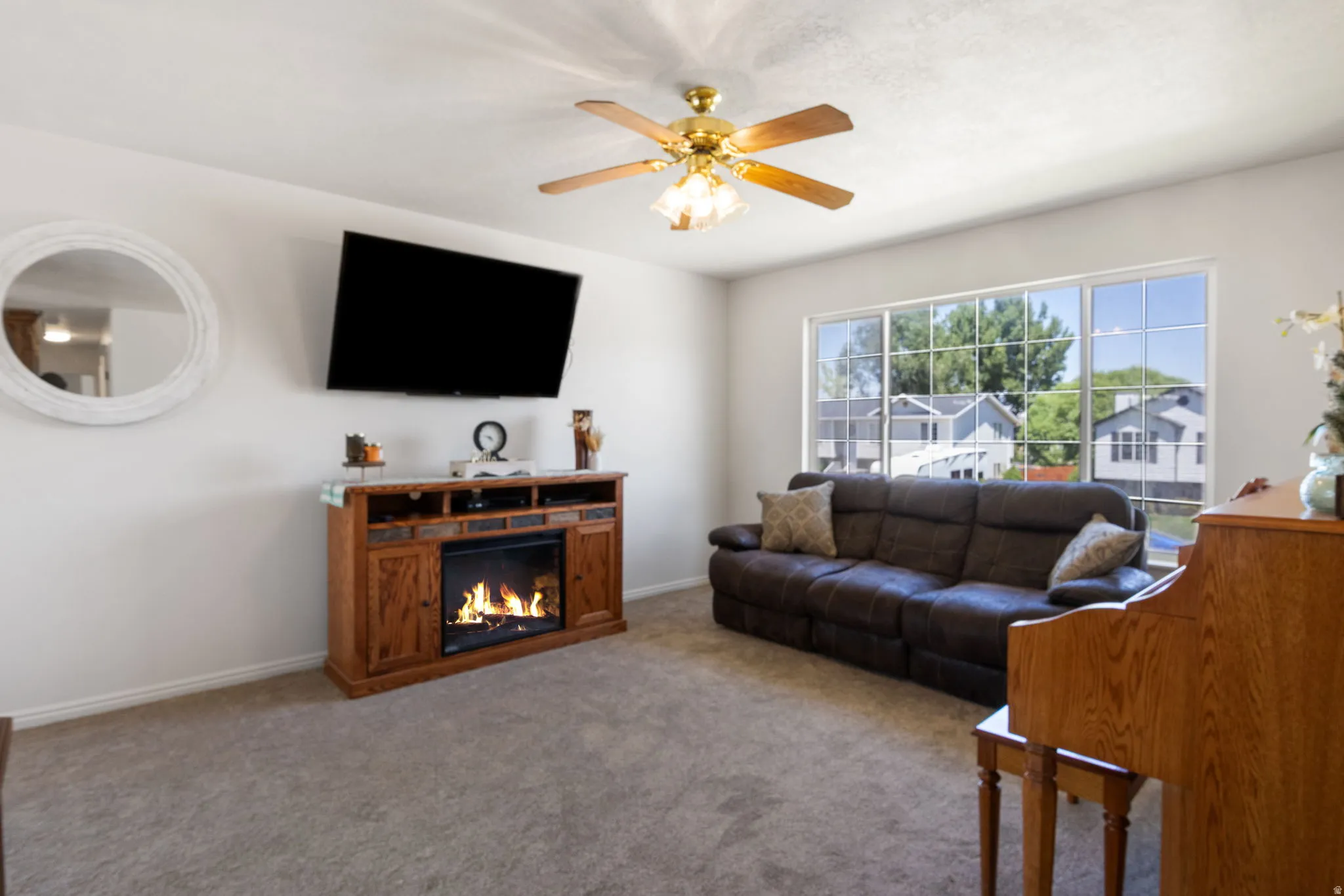 Living area featuring neutral carpeting, a white wall finish, a ceiling fan with light fixture, and a built-in media console with an electric fireplace