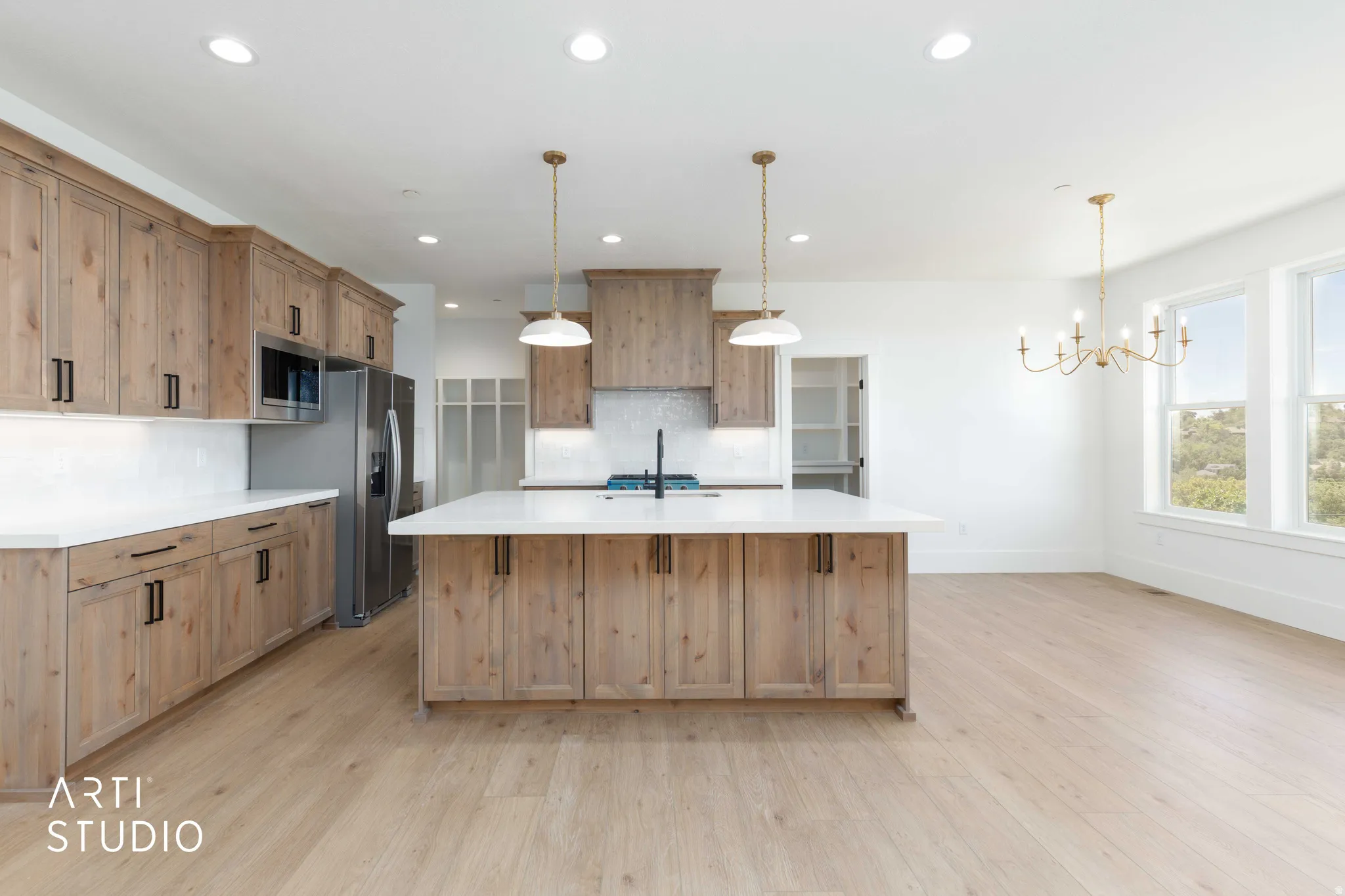 Open-concept kitchen featuring light wood-finish cabinetry, a large central island with a white countertop, stainless steel appliances, and wood-finish flooring