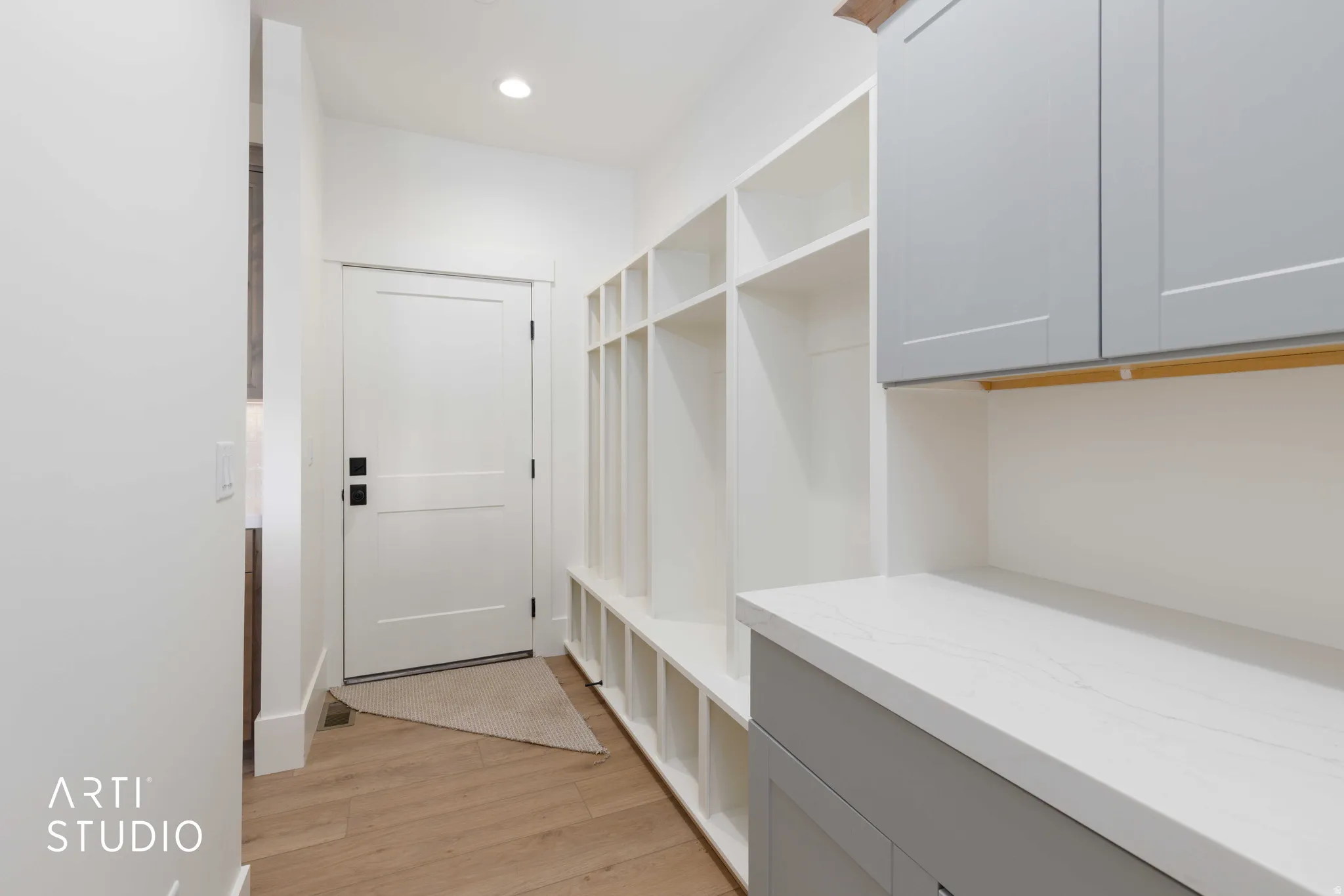 Entryway featuring built-in white cubbies, light wood-finish flooring, and a white flat-panel door with black hardware