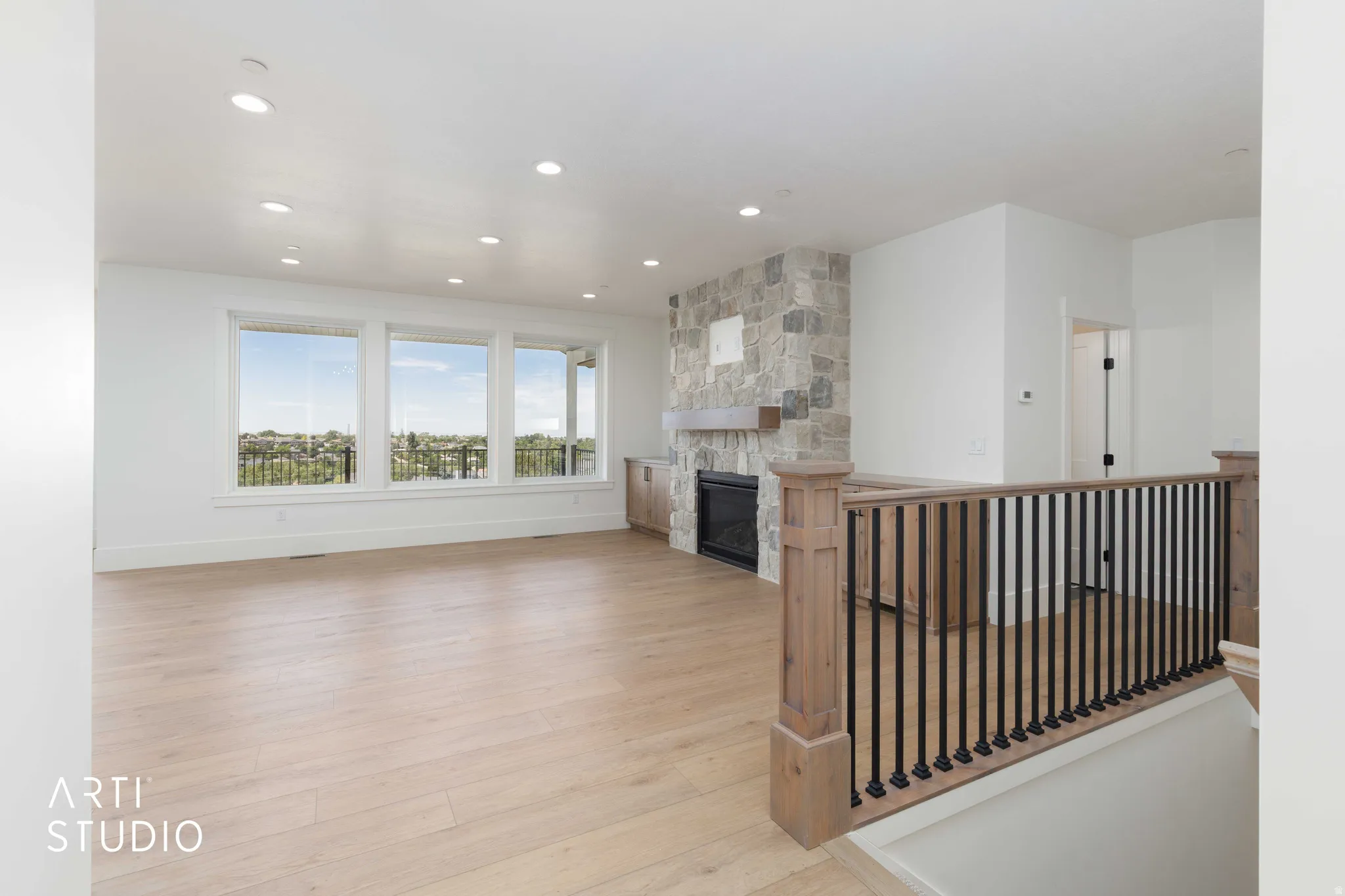 Spacious living area featuring light wood-finish flooring, a stone-clad fireplace with a wood mantle and built-in cabinetry, large windows offering expansive scenery, and recessed lighting