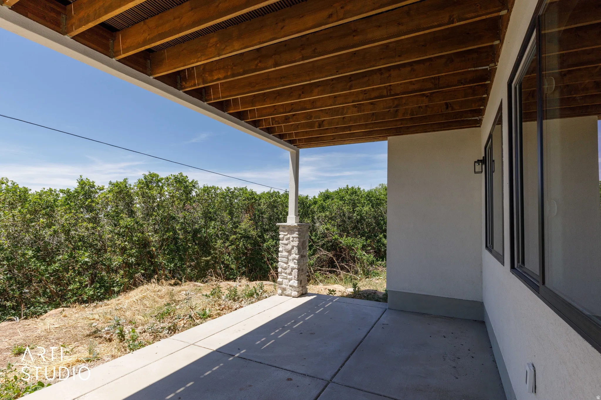 Covered concrete patio featuring a stone-clad pillar
