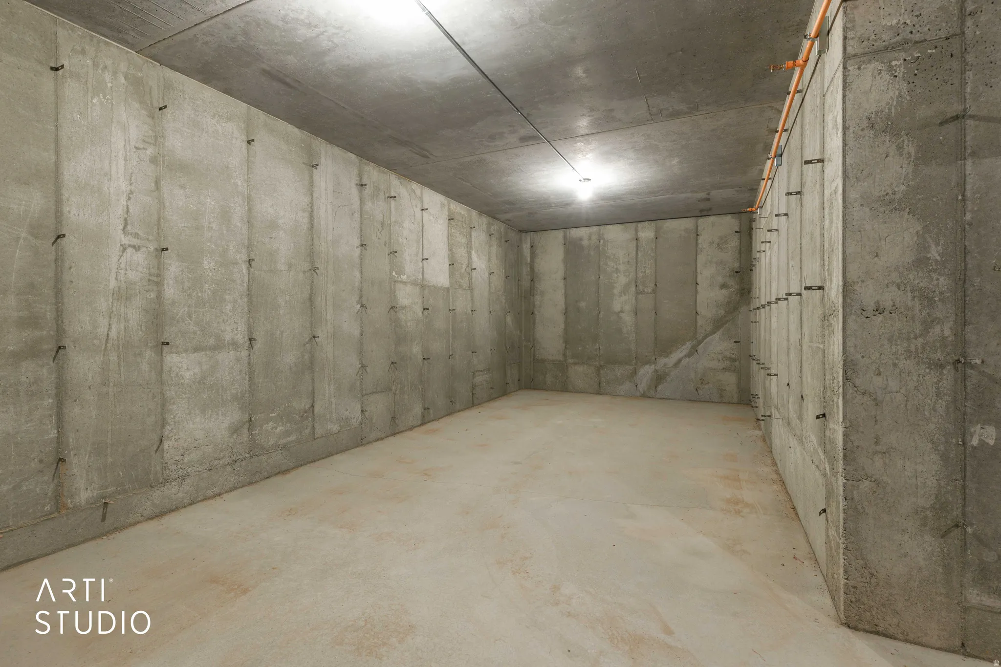 Concrete walls and ceiling featuring exposed wiring and a single overhead light fixture