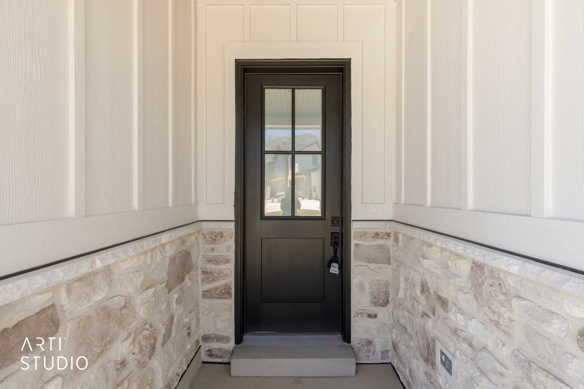 Modern black front door with clear glass panels, framed by white board and batten siding