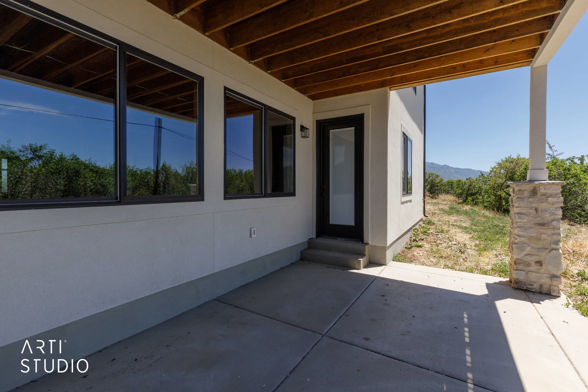 Covered concrete patio featuring a wood-finished ceiling, stone-accented support column, and multiple large windows