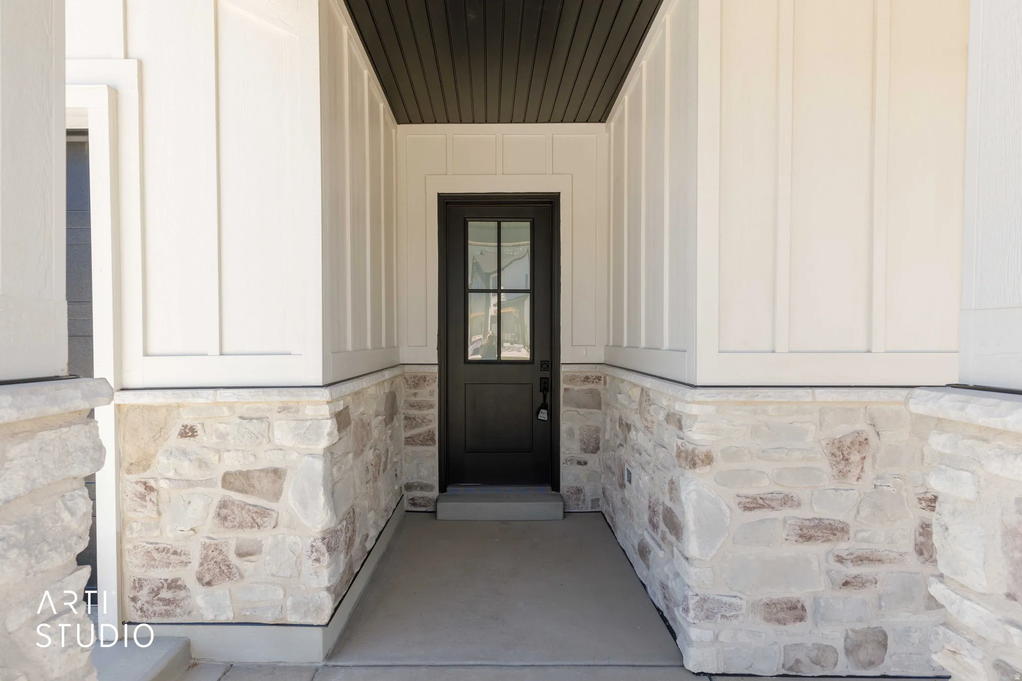 Covered entry featuring a dark-toned door with glass lites, stone veneer accents, vertical board-and-batten siding, and a dark-toned soffit
