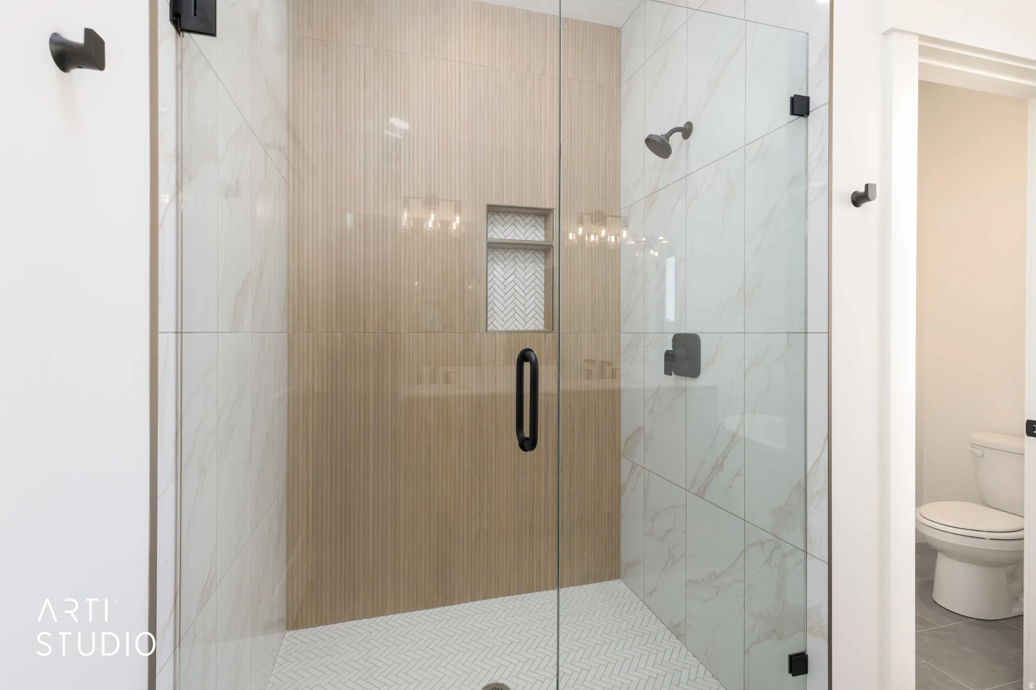 Glass-enclosed shower featuring white herringbone tile flooring, large-format marble-look wall tiles, and a recessed niche with herringbone tile