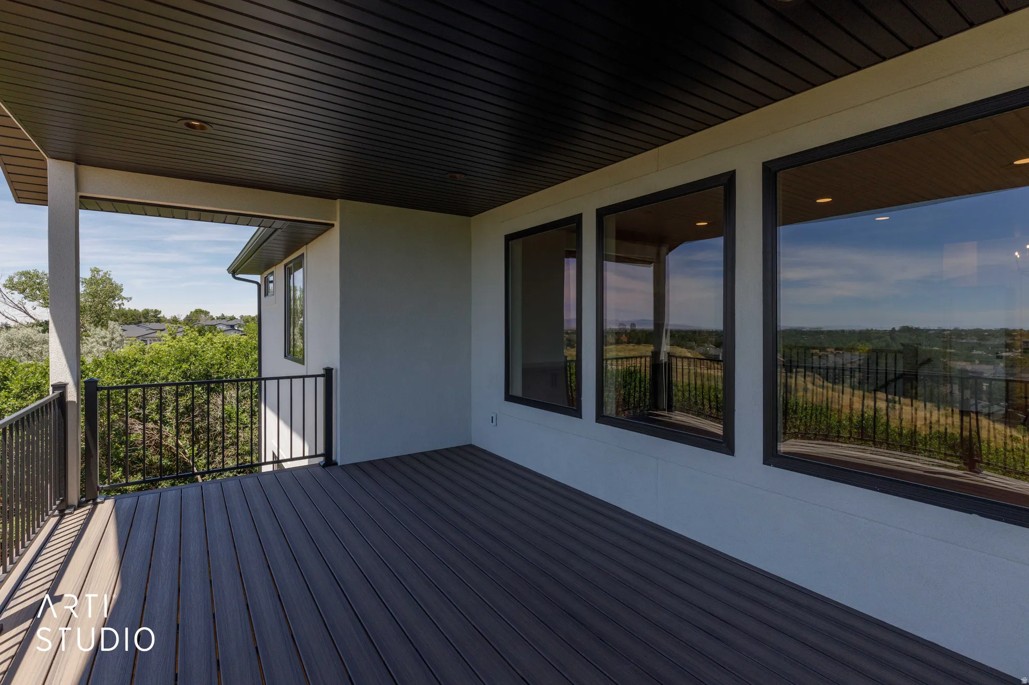 Covered outdoor deck featuring composite decking, black metal railings, recessed lighting, and expansive windows