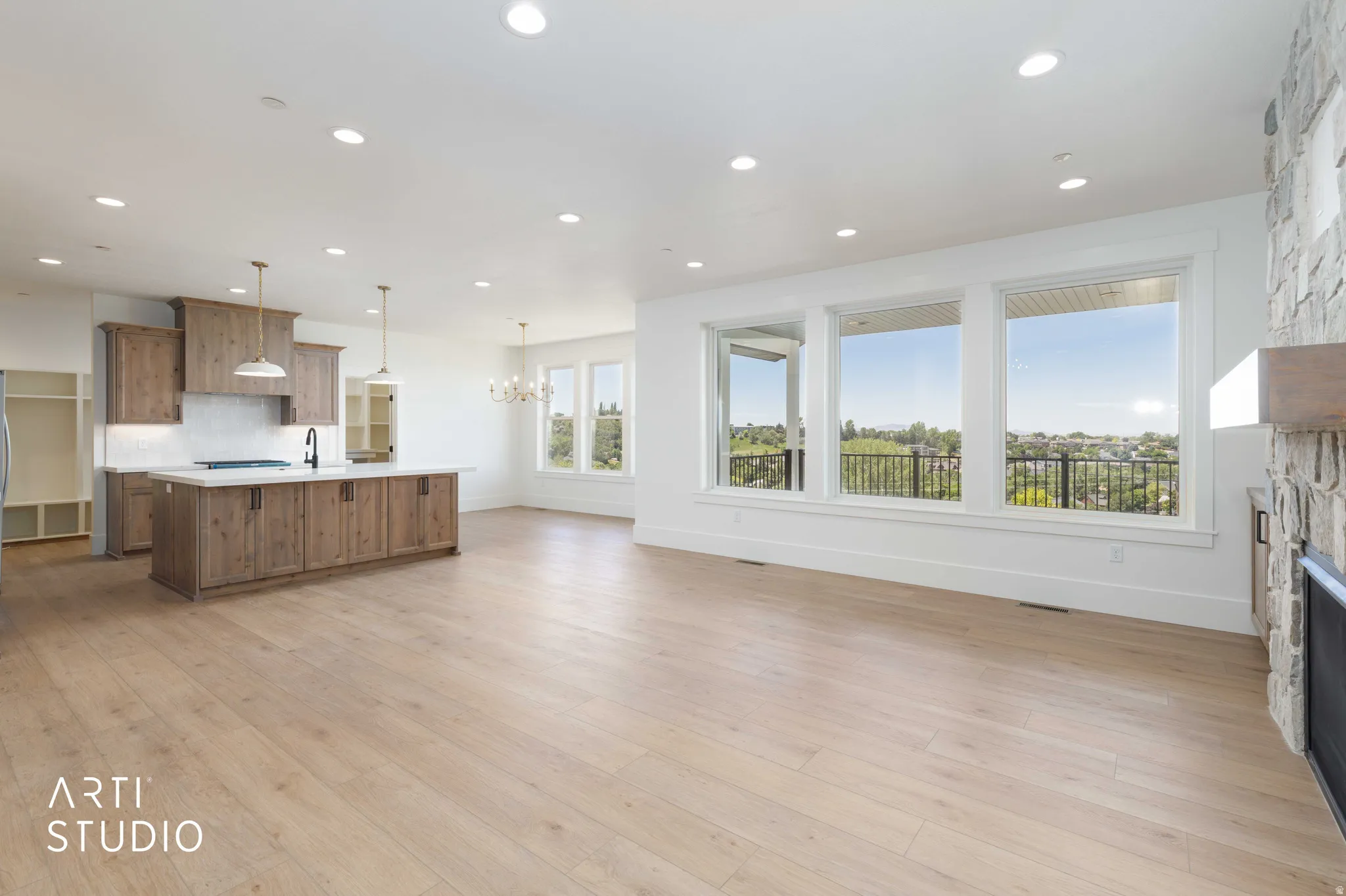 Open-concept living space featuring wood-finish flooring, a stone-clad fireplace, and expansive windows