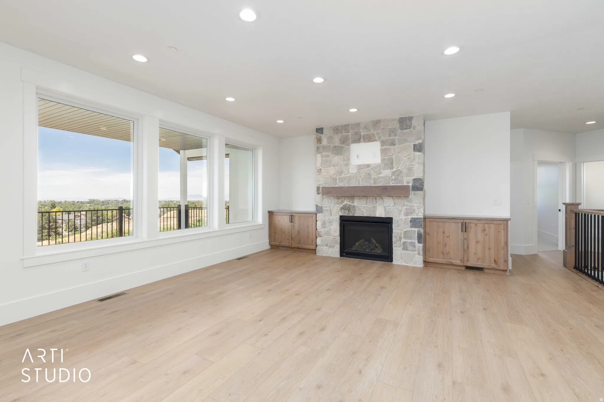 Spacious living area featuring light wood-finish flooring, a stone-clad fireplace with a wood mantle, and built-in cabinetry