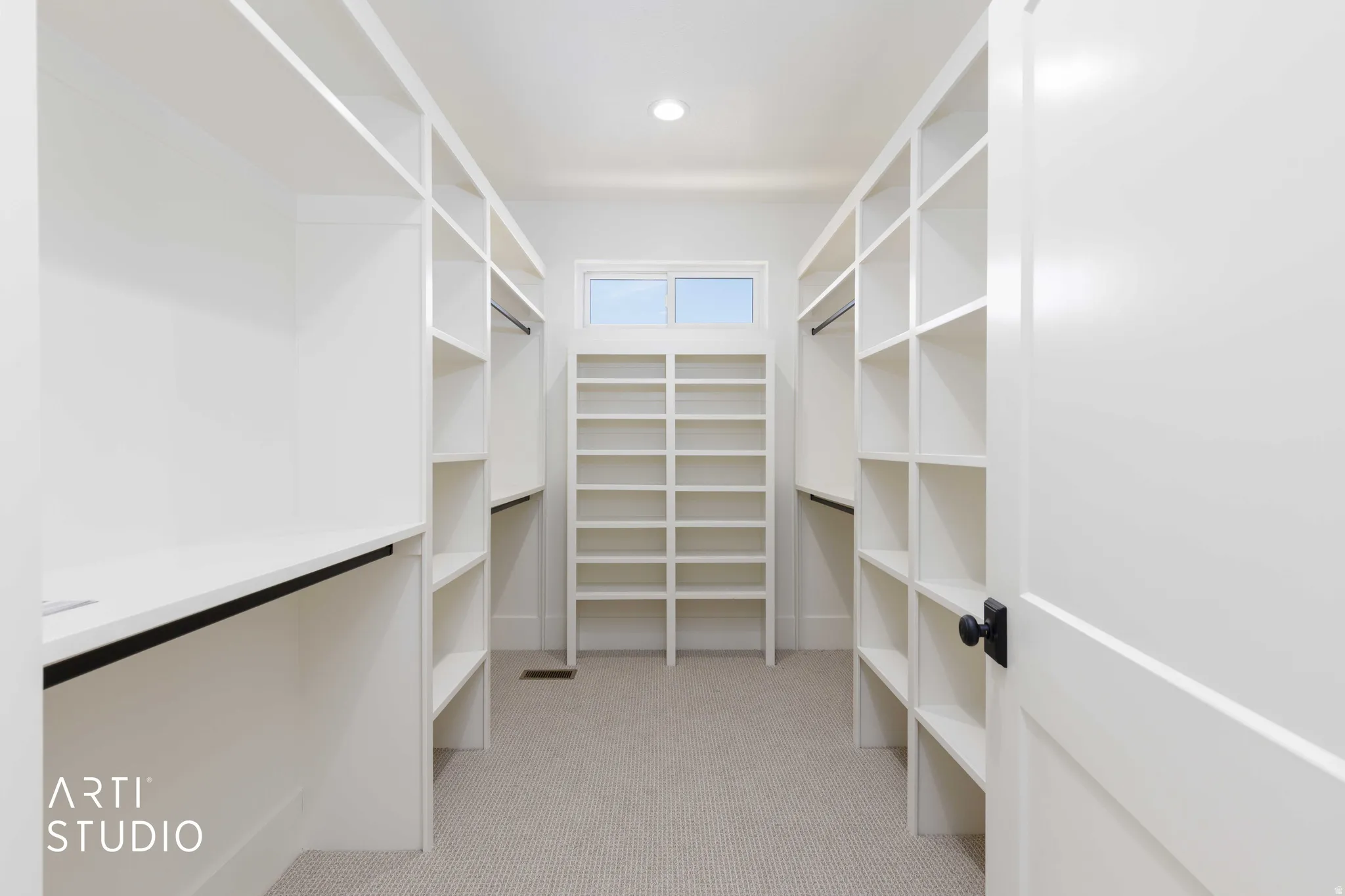 Spacious custom closet featuring extensive white built-in shelving, integrated hanging rods, and light-colored carpet flooring