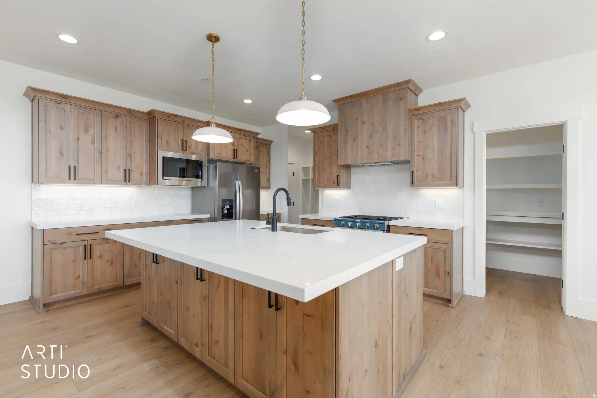 Kitchen featuring wood-finish cabinetry, stainless steel appliances, a center island with a white countertop, and a pantry with built-in shelving