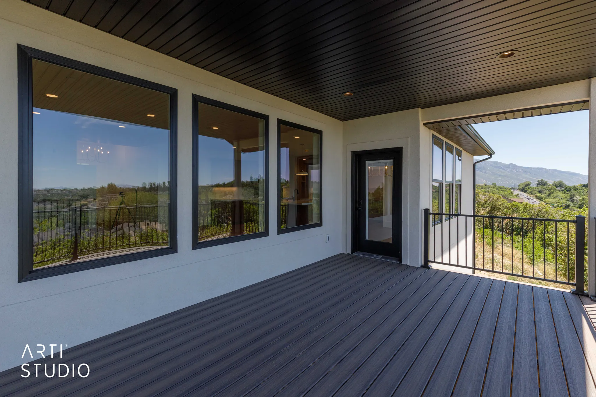 Expansive outdoor patio featuring composite decking, black metal railings, and a black framed glass door