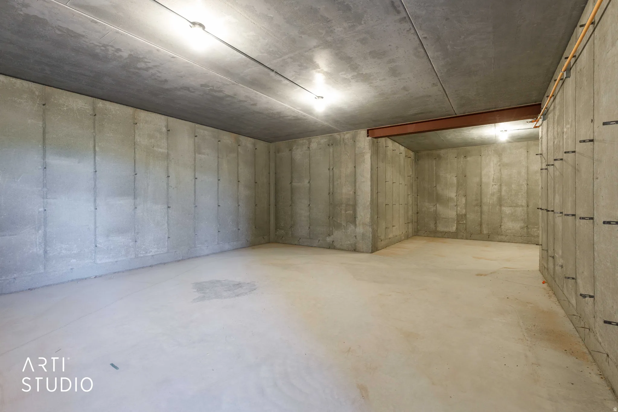 Spacious concrete room featuring concrete walls, concrete flooring, concrete ceiling, track lighting, and exposed structural beam