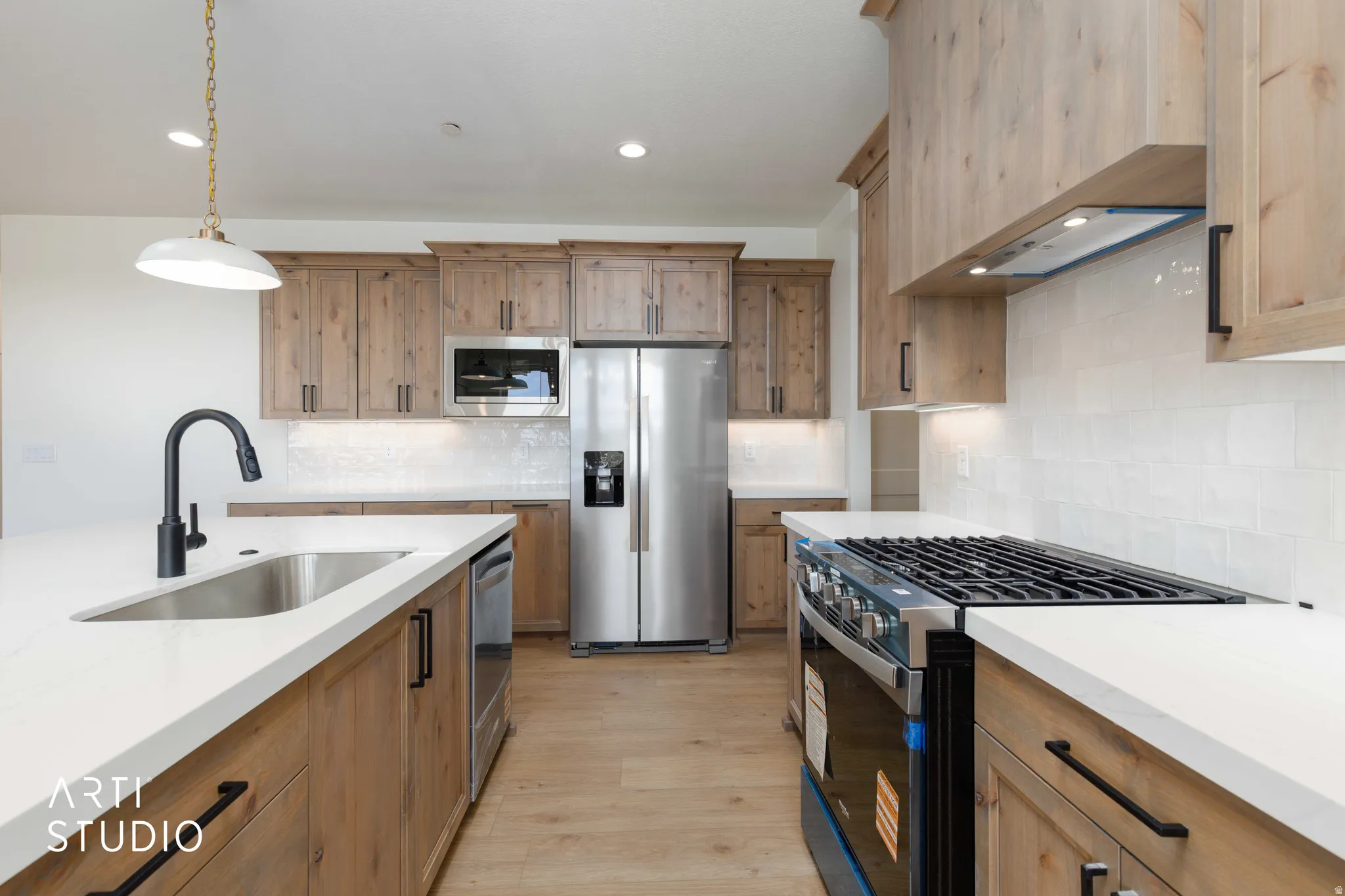 Modern kitchen with light wood-finish cabinetry, stainless steel appliances, white quartz countertops, and a subway tile backsplash