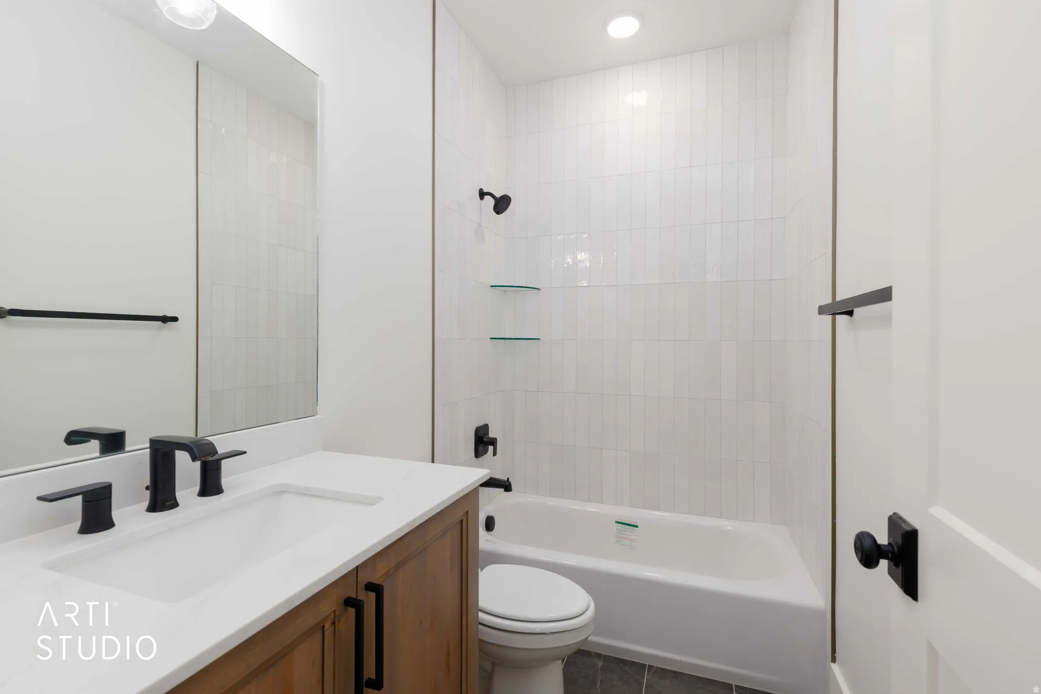 Bathroom featuring a wood-finish vanity with a white countertop and undermount sink, matte black fixtures, a built-in tub with white subway tile surround, and dark tile flooring