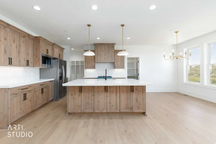 Open-concept kitchen featuring light wood-finish cabinetry, a large central island with a white countertop, stainless steel appliances, and wood-finish flooring