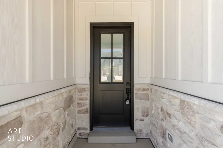Modern black front door with clear glass panels, framed by white board and batten siding