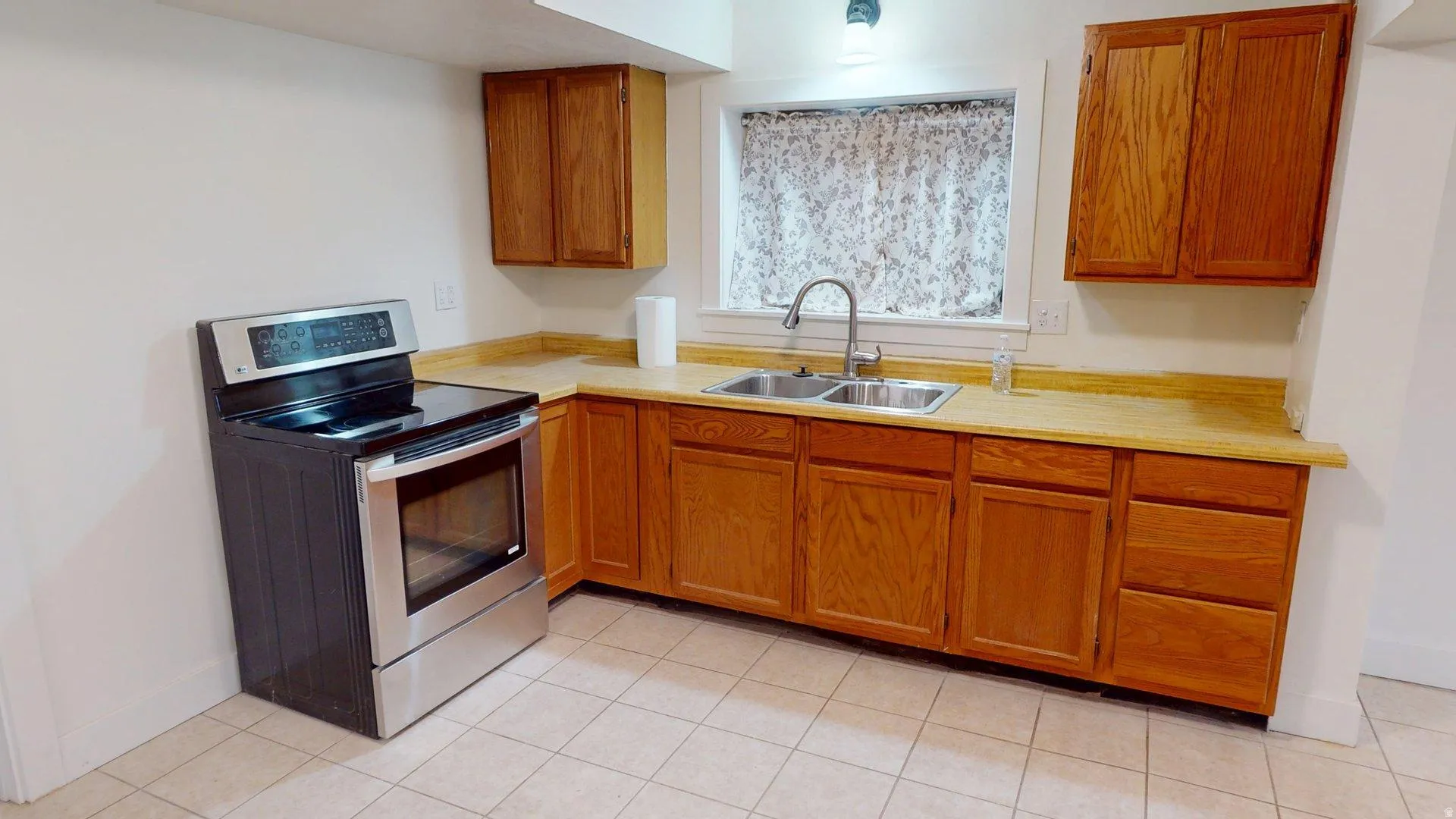 Kitchen featuring wood cabinetry, light-toned countertops, a stainless steel electric range, and a double basin sink with a gooseneck faucet