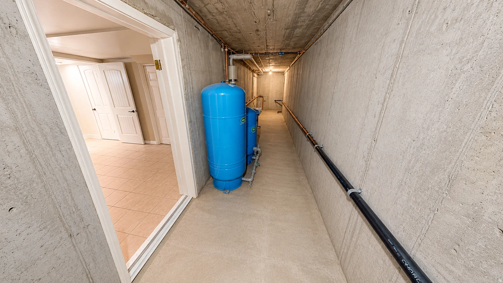Ai enhanced photo. Concrete-walled utility corridor featuring two large blue tanks and exposed piping