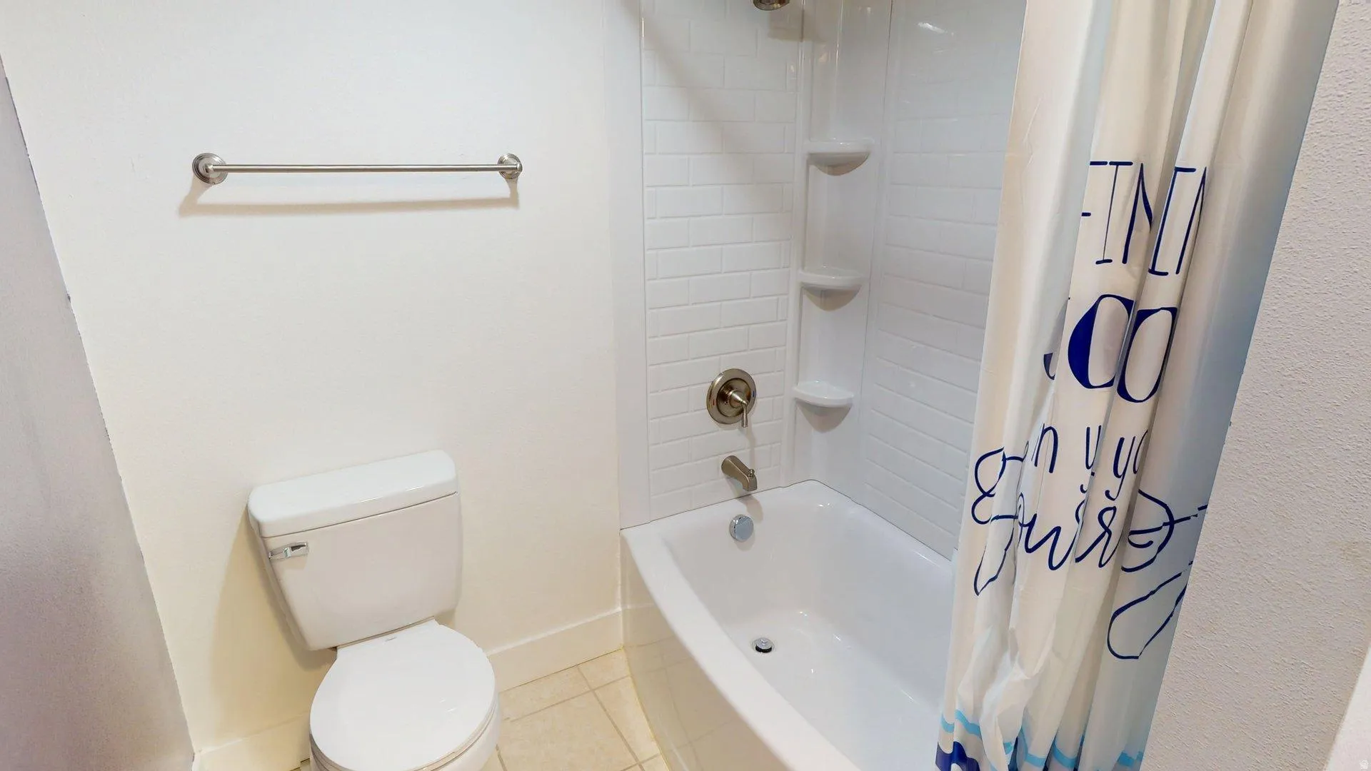 Bathroom featuring a white toilet, brushed nickel towel bar, and a white bathtub with subway tile surround and integrated shelving