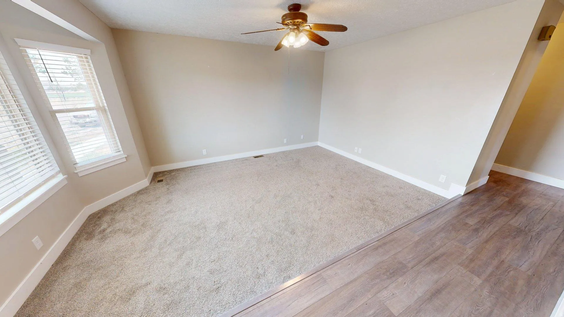 Spacious room featuring neutral carpeting, a ceiling fan with integrated lighting, and multiple windows with white blinds