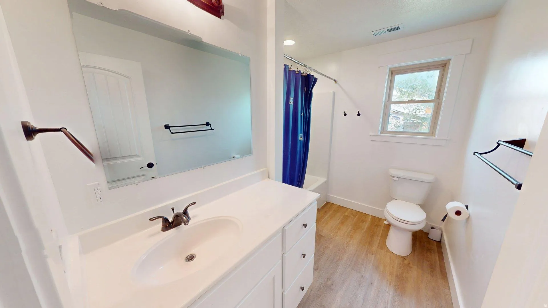 Bathroom featuring a vanity with an integrated sink, broad wall-mounted mirror, and wood-finish flooring