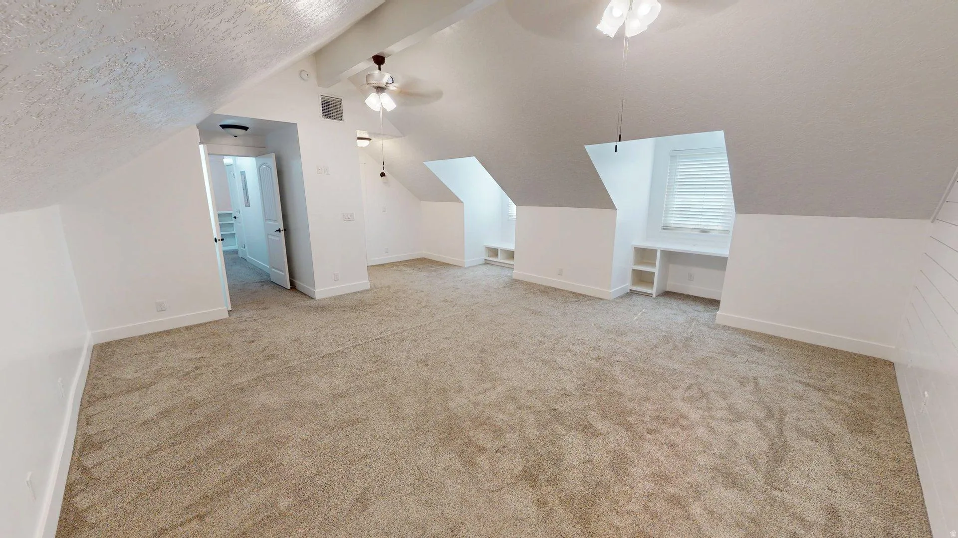 Expansive room with neutral carpeting and sloped ceilings