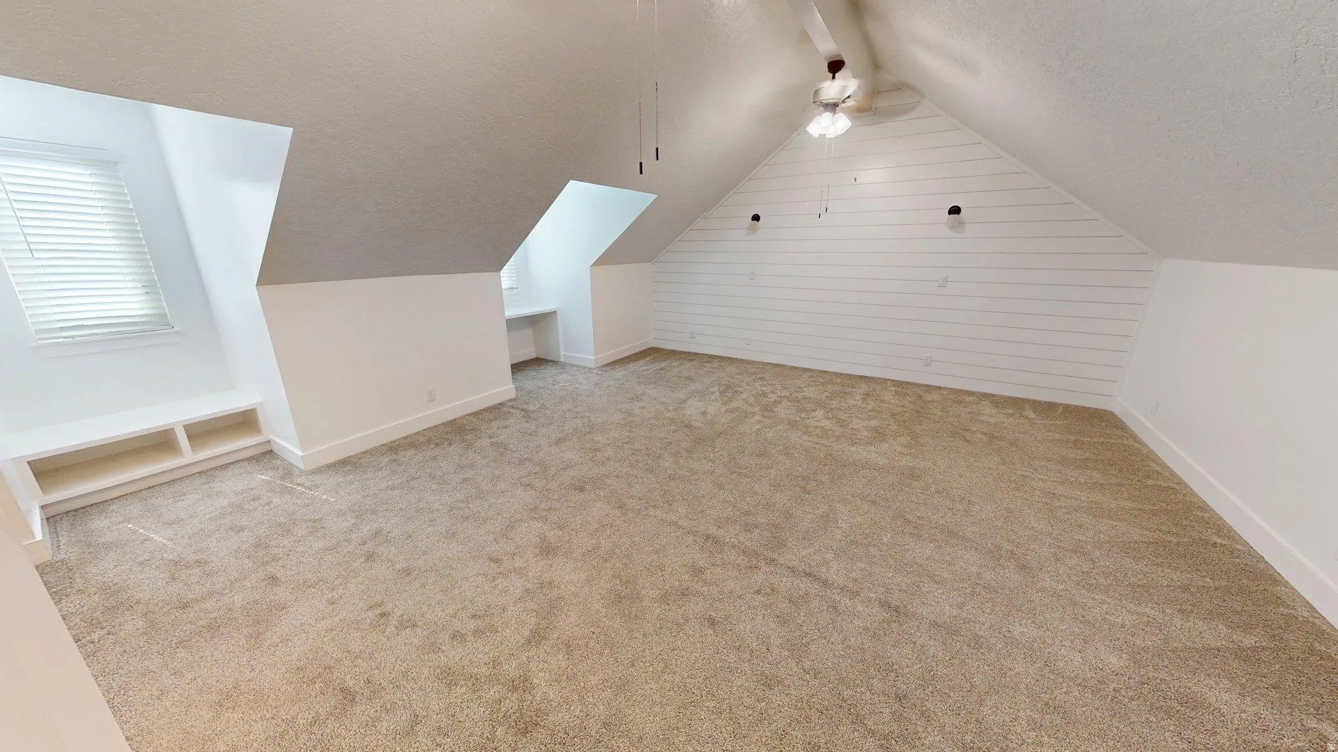 Expansive room featuring vaulted ceilings, shiplap accent wall, built-in window bench with shelving, and neutral carpeting