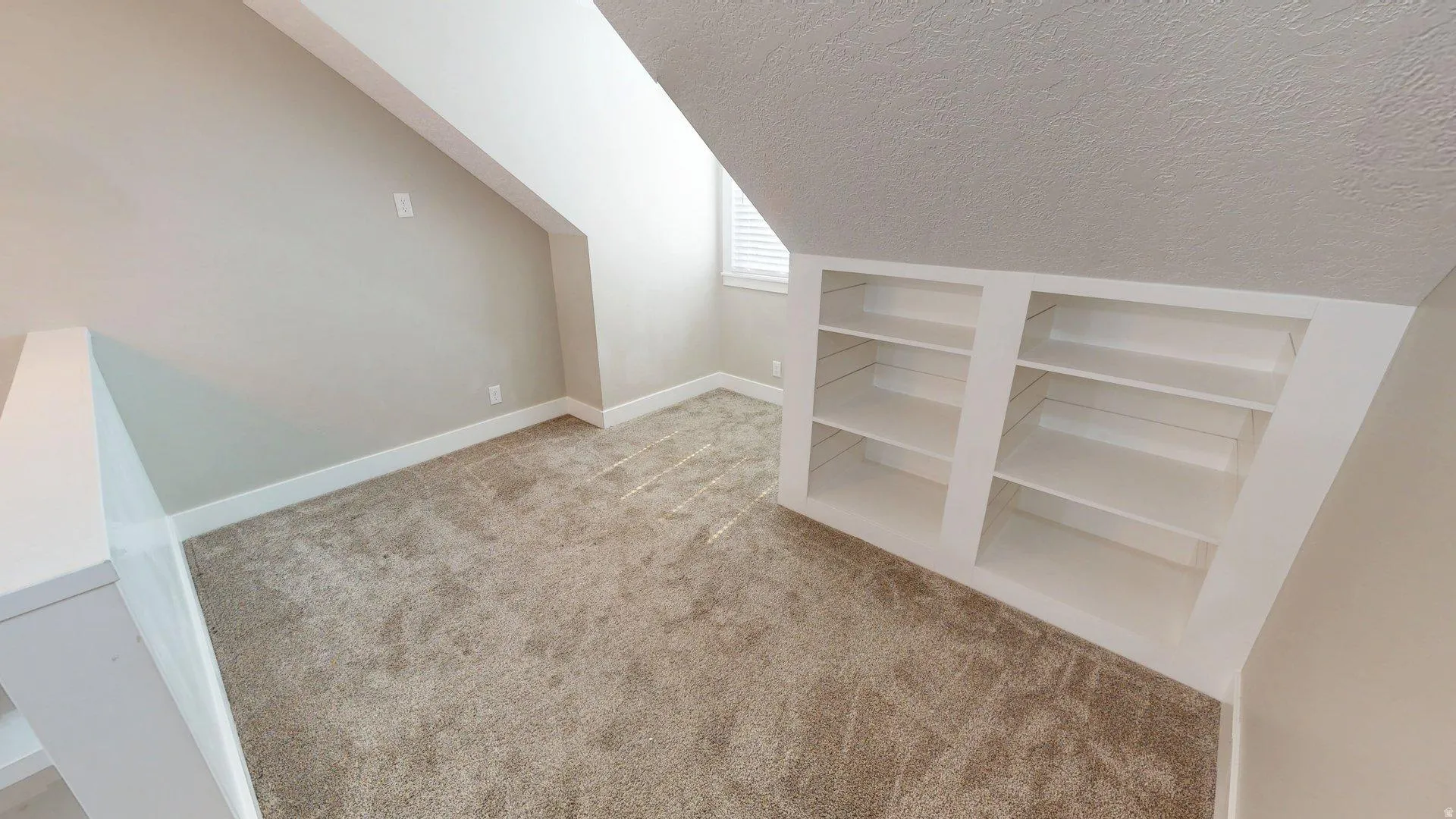Carpeted bonus room featuring built-in shelving, sloped ceilings, and a window with blinds