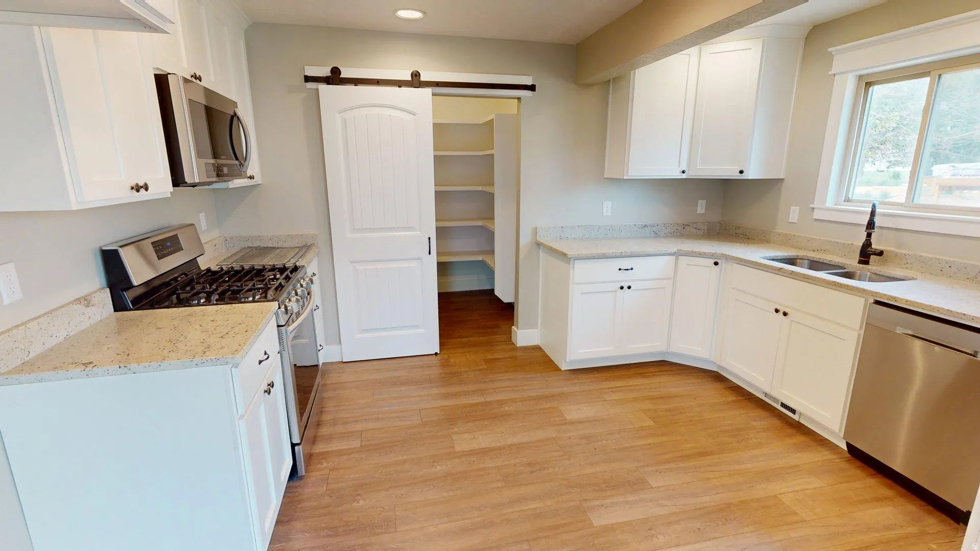 Kitchen featuring white cabinetry, light-toned countertops, stainless steel appliances, and wood-finish flooring