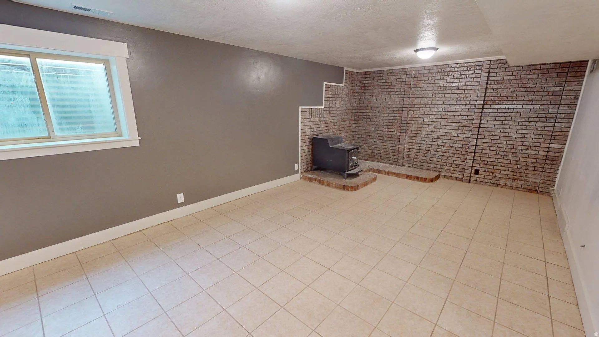 Spacious room with large tile flooring and a brick accent wall