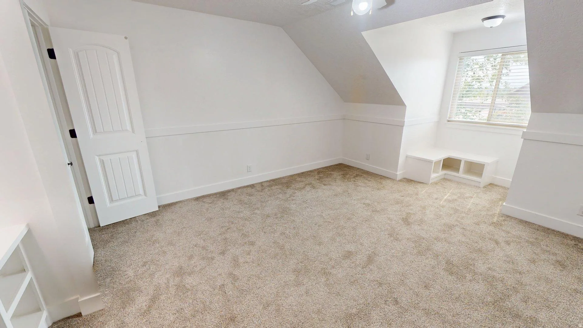Carpeted interior with sloped ceilings, a built-in window bench, a window with blinds, and a paneled door