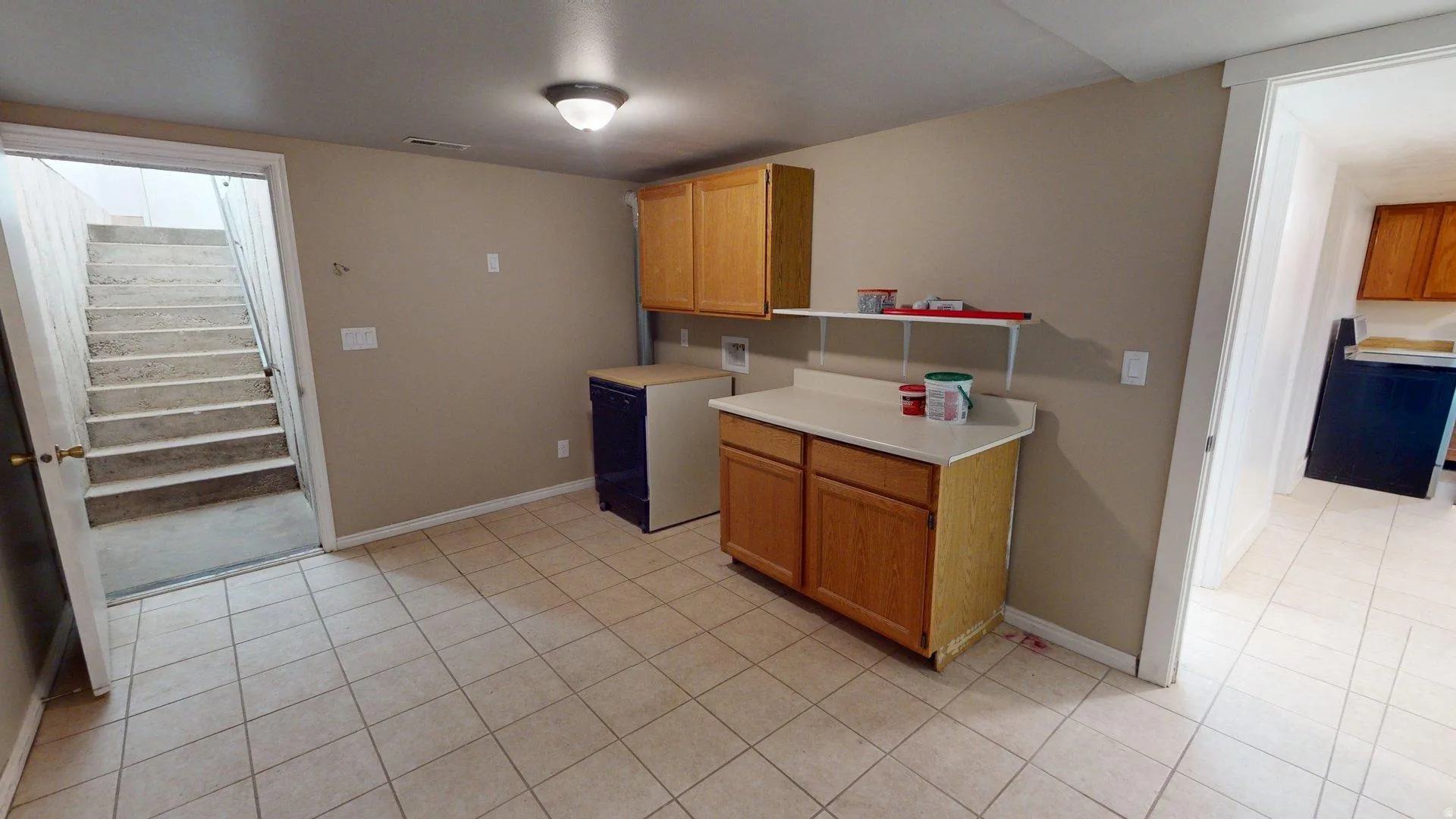 Utility area featuring tiled flooring, wood-finish cabinetry, and a light-toned countertop