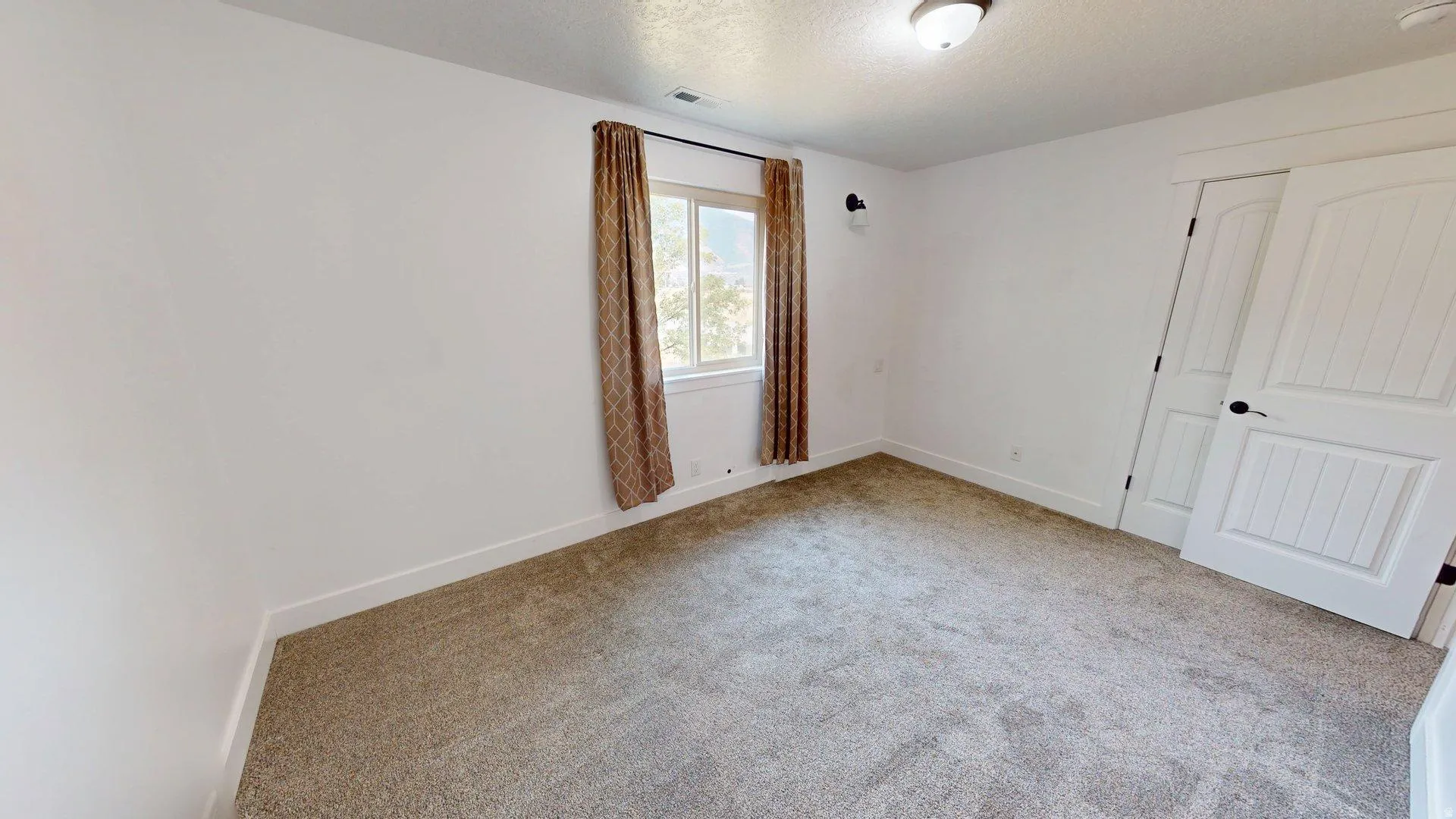 Carpeted room featuring a single window, white baseboards, and a white interior door with a black handle